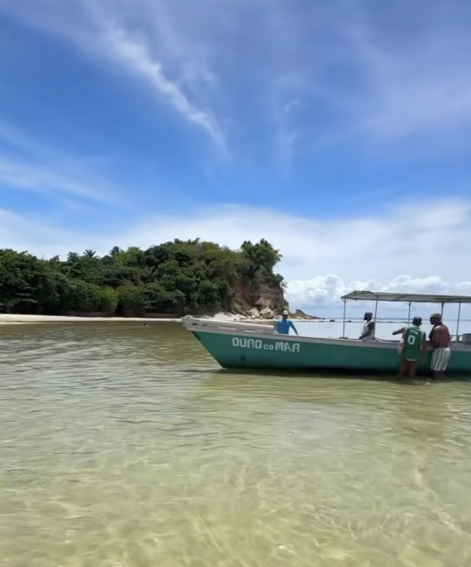 Barco Ouro do Mar em águas transparentes com ilhota tropical ao fundo