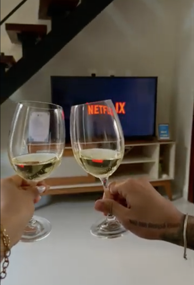 Duas taças de vinho branco brindando em frente à TV com Netflix no Studio Moderno, escada do loft ao fundo
