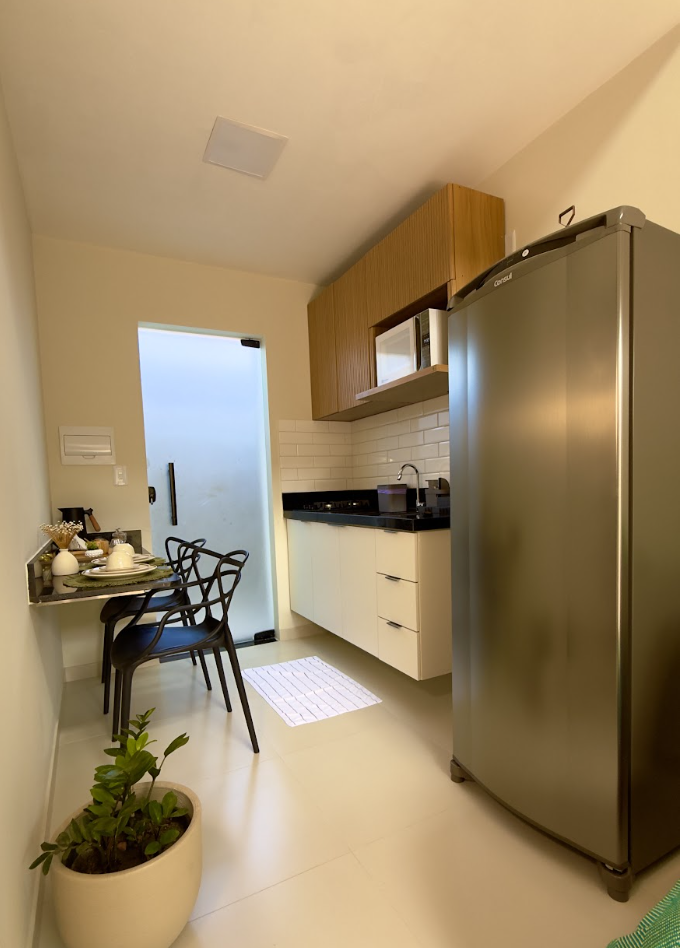 Cozinha compacta com geladeira inox, armários de madeira, bancada de granito e mesa de jantar com cadeiras pretas