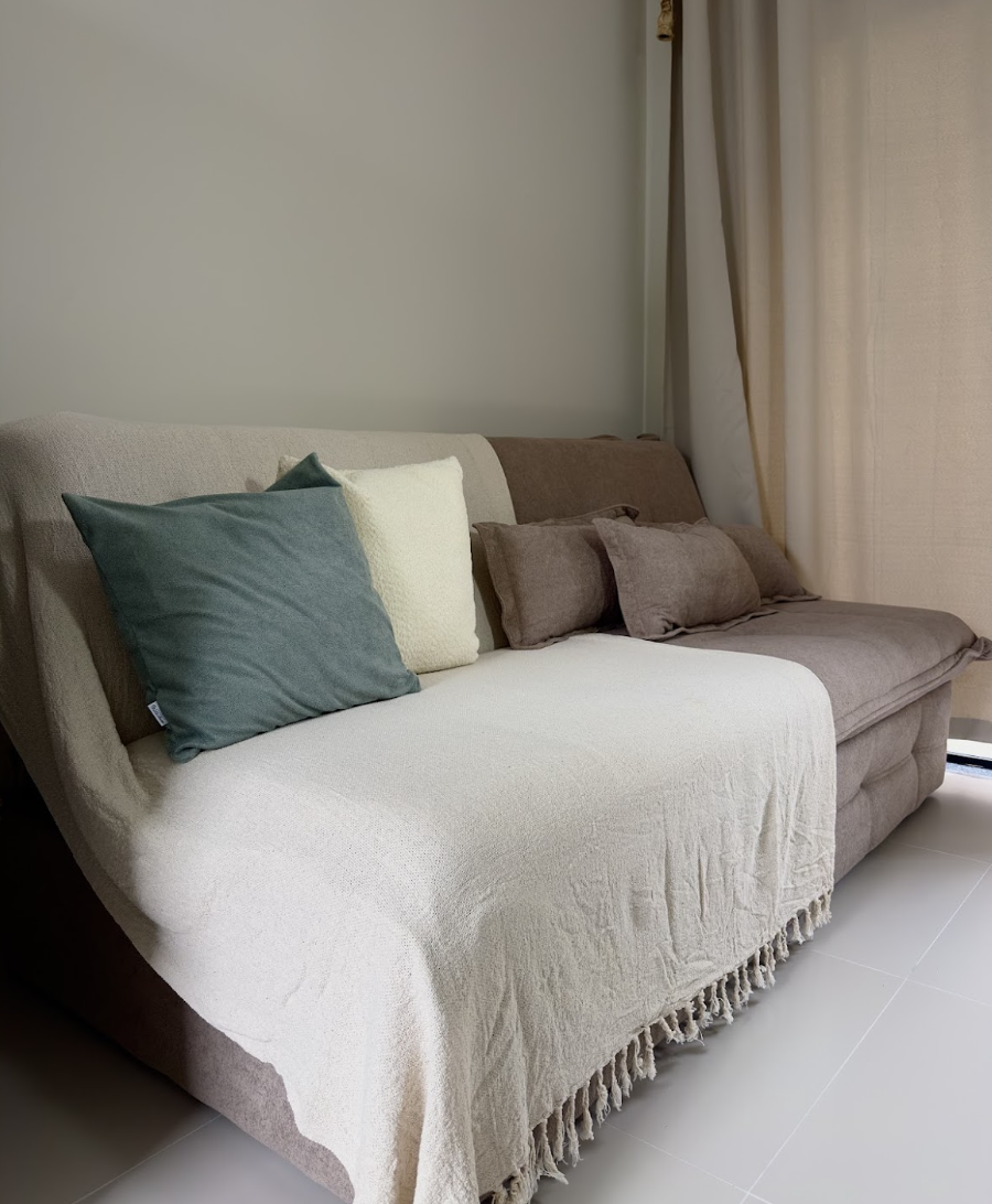 Sofá-cama bege com almofadas teal e bege e cortinas longas de linho ao lado da janela