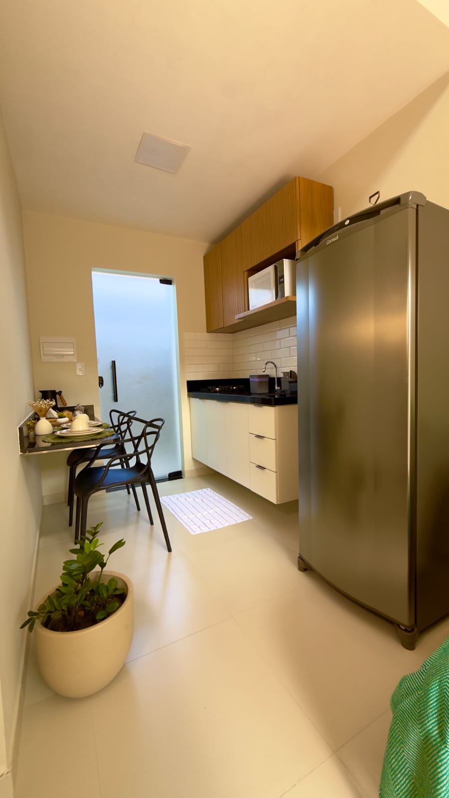 Cozinha compacta com geladeira inox, armários de madeira ripada e mesa de jantar com cadeiras pretas