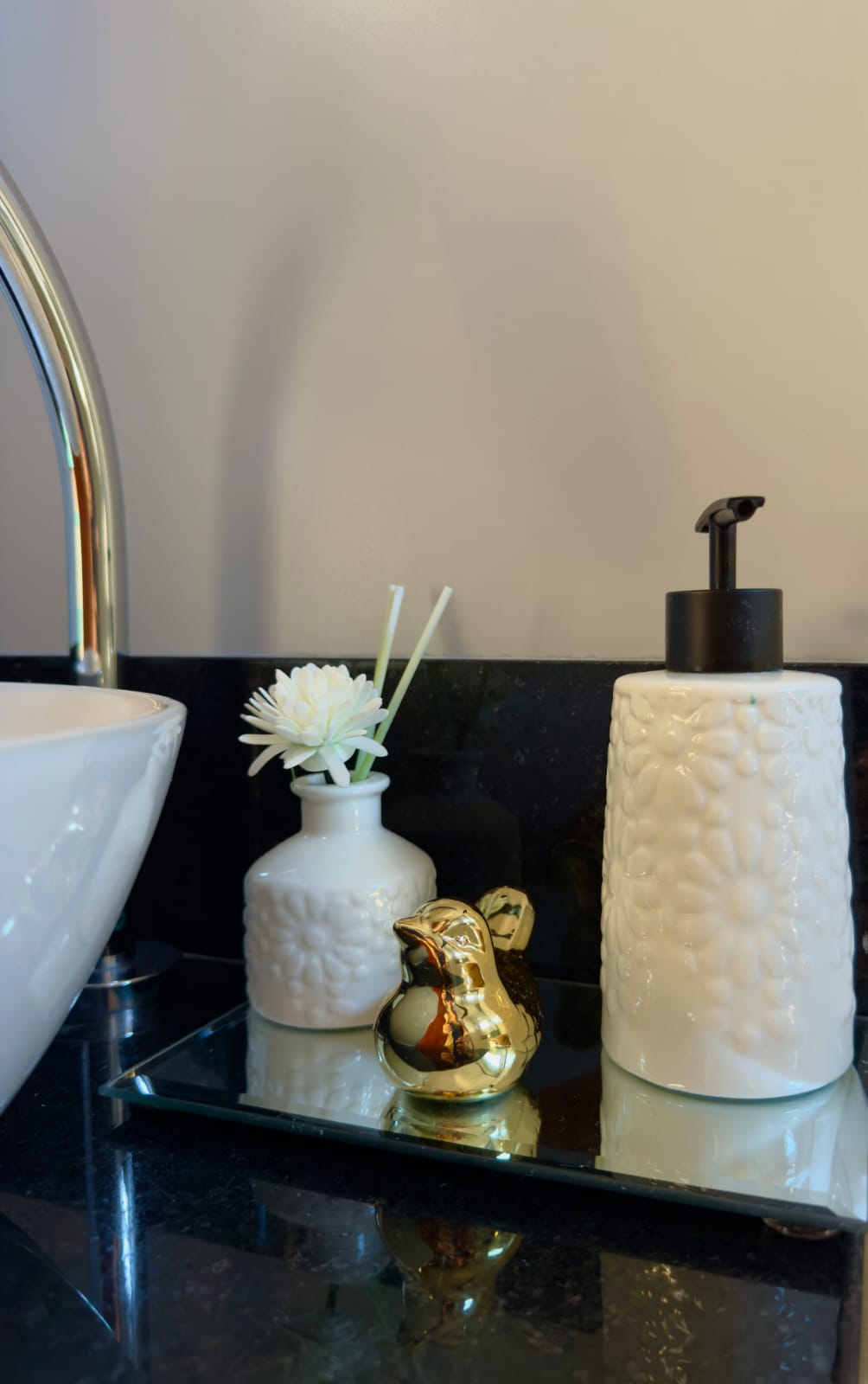 Detalhe do banheiro com difusor de flor branca, passarinho dourado e saboneteira no granito